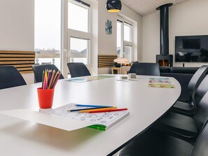 A modern meeting room with a white table, black chairs, and a fireplace. - 5 Star Holiday Home in Lokken (Lokken)