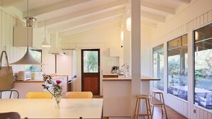 Une cuisine moderne dotée d’un îlot central, de planchers en bois et de grandes fenêtres offrant une vue sur l’extérieur.