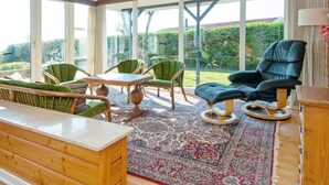 A sunlit room with a wooden ceiling, large windows, a green sofa, a dining table, and a patterned rug. - 6 Person Holiday Home in Borkop (Borkop)
