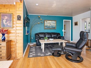 A room with a teal wall, wooden paneling, a black leather sofa, a wooden coffee table, a black leather chair, and a painting of a ship. - 6 Person Holiday Home in Borkop (Borkop)