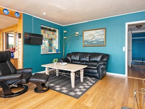 A room with a black leather sofa, a dining table, a TV on the wall, and a window with a view of the sea. - 6 Person Holiday Home in Borkop (Borkop)