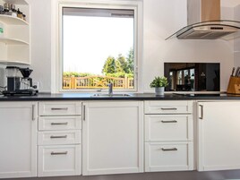Una cocina moderna con armarios blancos, estufa empotrada y ventana con vistas a una terraza de madera.