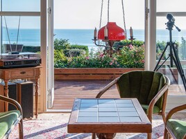 Una habitación con vista al océano, una radio antigua, un trípode y una silla verde.
