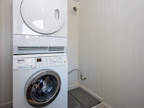 A front-loading washing machine with a control panel, a dryer above it, and a small window vent on the wall. - 6 Person Holiday Home in Borkop (Borkop)