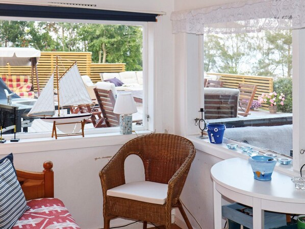 A room with a wicker chair, a small table with a lamp, and a view of outdoor furniture through a window. - 9 Person Holiday Home in Frandefors (Frändefors)