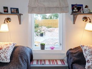 Una habitación acogedora con dos camas, una ventana que da a un jardín y objetos decorativos en estantes.