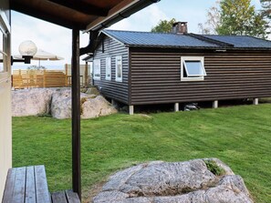 A wooden cabin with a metal roof, a grassy yard, and large rocks. - 9 Person Holiday Home in Frandefors (Frändefors)