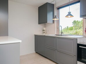 A kitchen with grey cabinets, a white countertop, a coffee maker, and a window with a view of greenery.