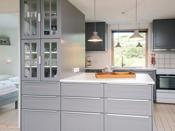A modern kitchen with grey cabinetry, a central island, pendant lighting, and a view through the window.