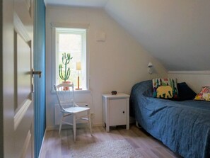 A bedroom with a sloped ceiling, a bed with a blue blanket, a white chair, a small bedside table, a lamp, and a potted cactus by the window. - 6 Person Holiday Home in Aplared-by Traum (Aplared)