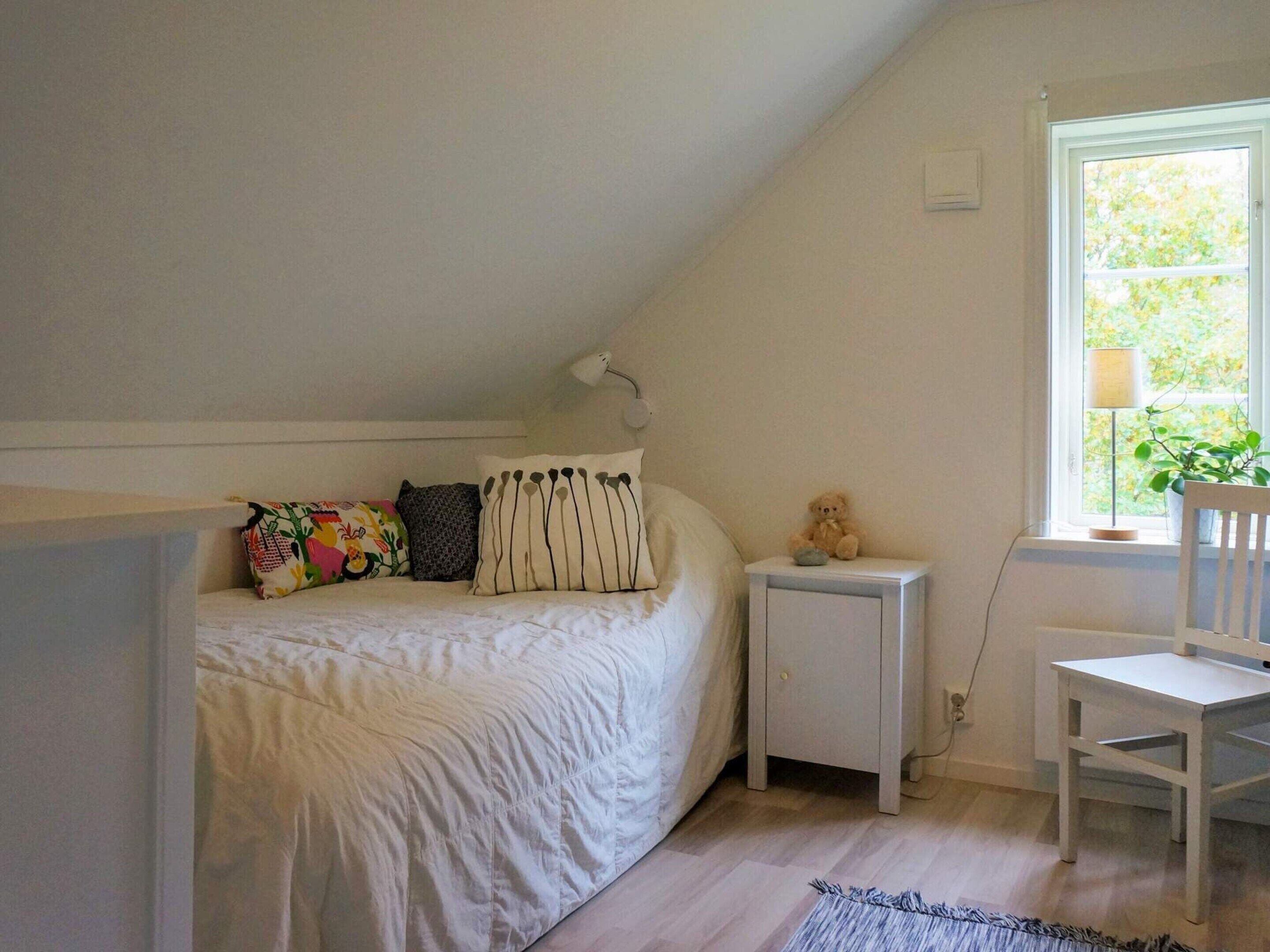 Makuuhuone, jossa on sänky, yöpöytä, tuoli, ikkuna, josta on näkymä vehreään maisemaan, ja lamppu.