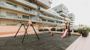 A playground with swings and a slide in front of a modern apartment building.