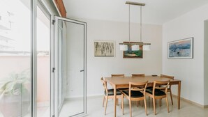 A dining area with a wooden table and chairs, a hanging light fixture, and two framed artworks on the walls.