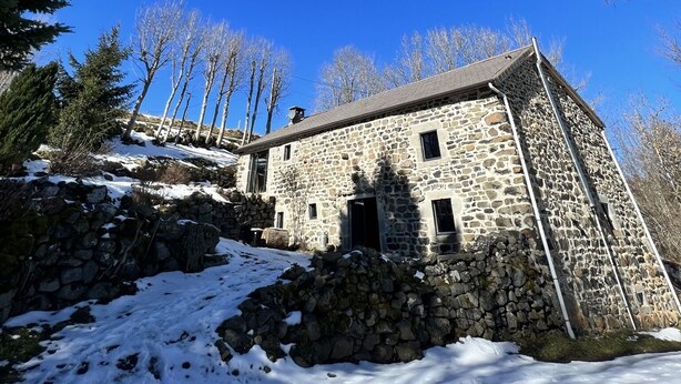 A stone building with a sloped roof, surrounded by snow and trees.