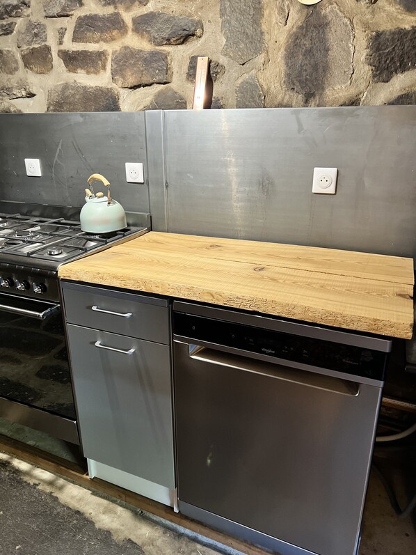 A kitchen with a wooden countertop, stainless steel appliances, and a stone wall. - Au bout d'un chemin, La Coustete (Saint-Front)