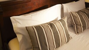 Una cama con cabecera de madera, almohadas blancas y a rayas, y una pared lisa al fondo.