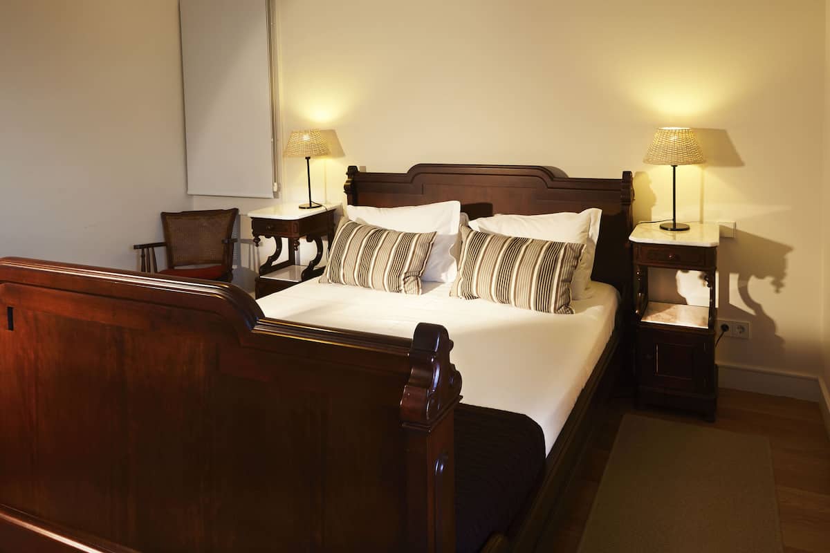 A neatly made bed with a wooden headboard, two bedside tables with lamps, and a chair.