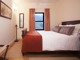 Un dormitorio con una cama grande, una ventana con cortinas, una mesita de noche y una lámpara.