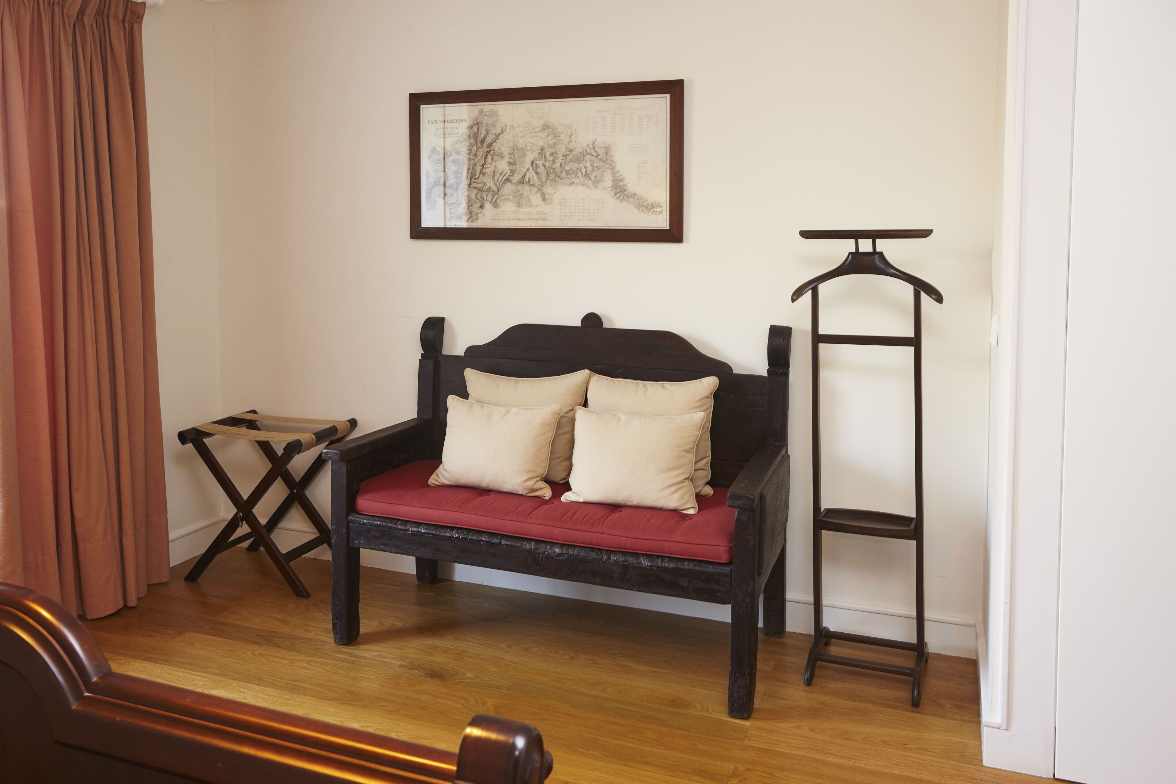Een kamer met een houten bed, een klein tafeltje, een kapstok en een lijst met een kunstwerk aan de muur.