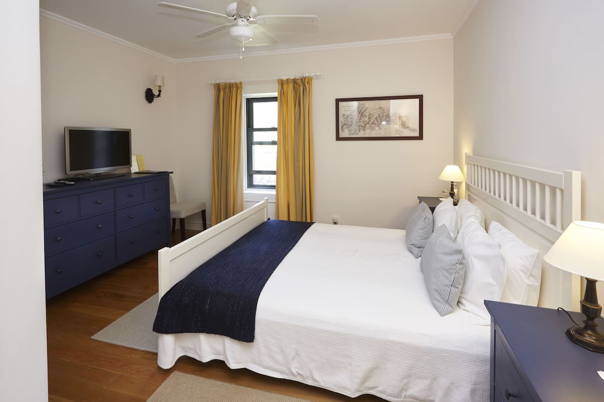 A neatly arranged bedroom with a bed, bedside table, lamp, and a TV on a dresser.