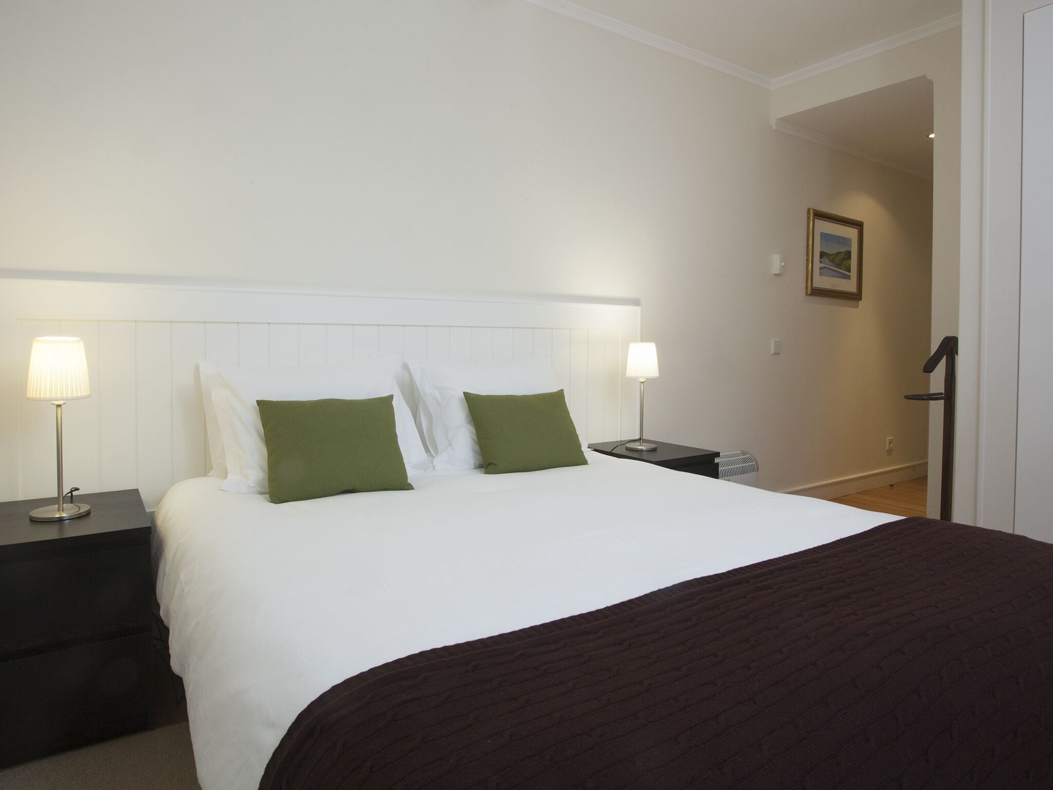 Una habitación de hotel con una cama grande, dos mesitas de noche y una mesita auxiliar.