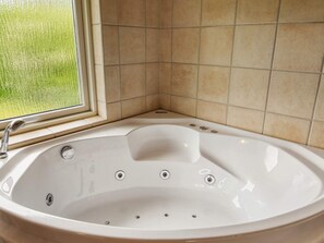A bathroom with a large bathtub, a window, and beige tiled walls. - 5 Person Holiday Home in Nakskov (Nakskov)
