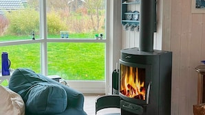 A cozy living room with a large window, a black wood-burning stove, and a blue sofa. - 5 Person Holiday Home in Nakskov (Nakskov)