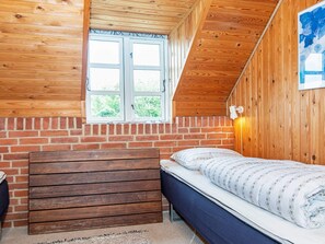 A small, cozy room with a sloped ceiling, a wooden bench, a single bed, and a window with a view of greenery. - 6 Person Holiday Home in Ringkobing (Ringkobing)