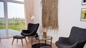 A modern living room with a glass table, two black armchairs, and a small stool.