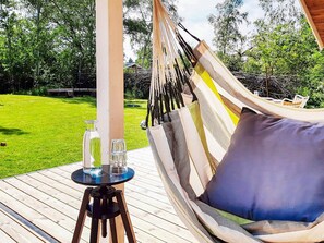 A hammock chair with a cushion, a small table with two glasses, and a bottle on a deck. - 5 Star Holiday Home in Dannemare (Dannemare)