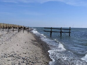 A beach with a wooden fence, pebbles, and waves. - 5 Star Holiday Home in Dannemare (Dannemare)