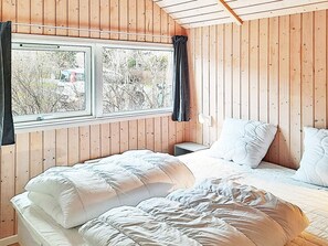 A bedroom with two beds, wooden walls, a window with curtains, and a bedside table. - 5 Star Holiday Home in Dannemare (Dannemare)