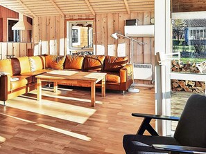 A living room with a wooden floor, a sectional sofa, a coffee table, and a lamp. - 5 Star Holiday Home in Dannemare (Dannemare)