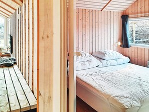 A wooden room with a bed, a window with a curtain, and a view of trees outside. - 5 Star Holiday Home in Dannemare (Dannemare)