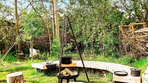 An outdoor cooking area with a wood-fired stove, a hanging pot, and a bench. - 5 Star Holiday Home in Dannemare (Dannemare)
