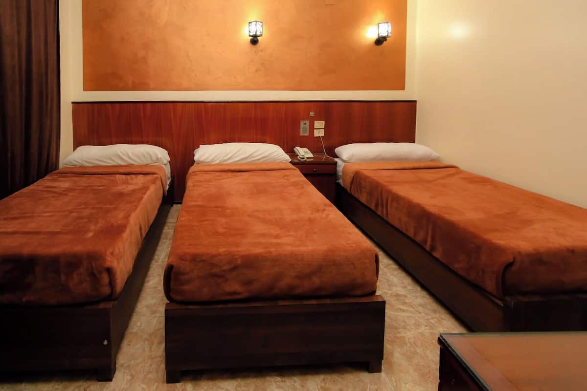 Ein Hotelzimmer mit drei Einzelbetten, einem Holzkopfstück und zwei Wandleuchten.
