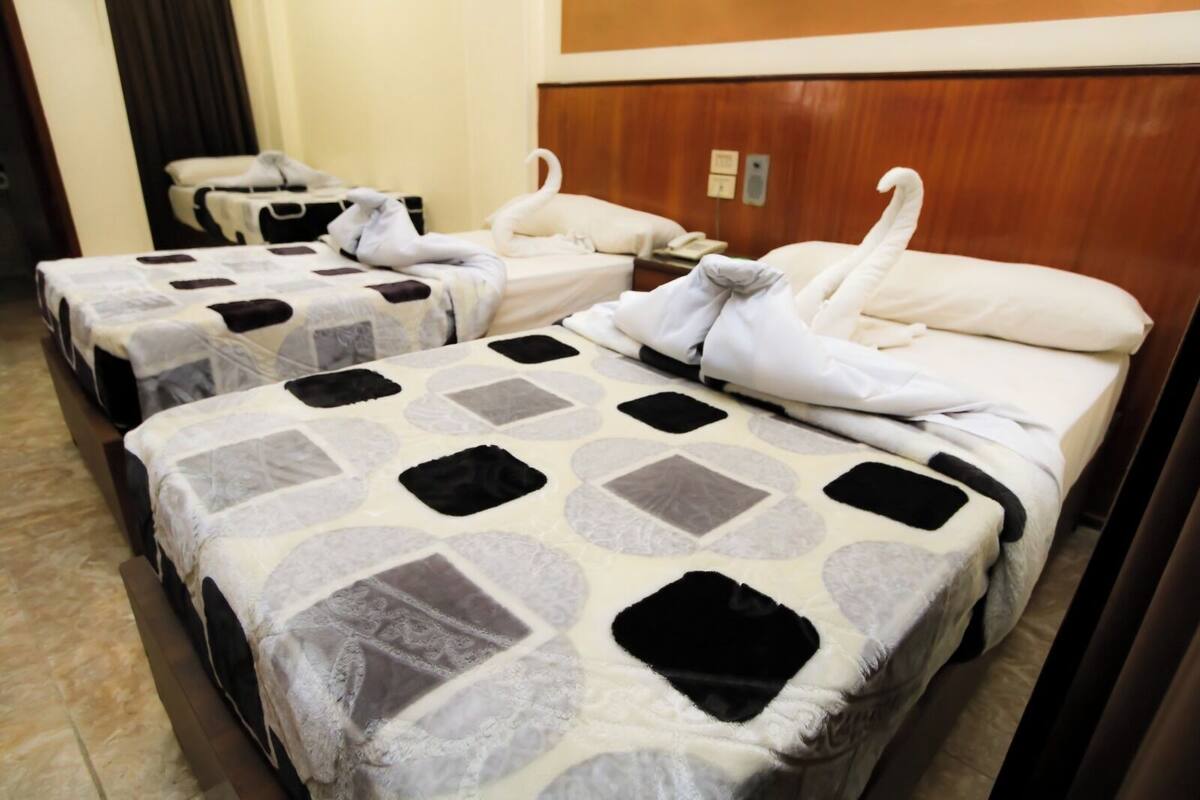 Ein Hotelzimmer mit drei Betten, jedes mit einer geblümten Tagesdecke und einem schwanenförmigen Kopfkissen.