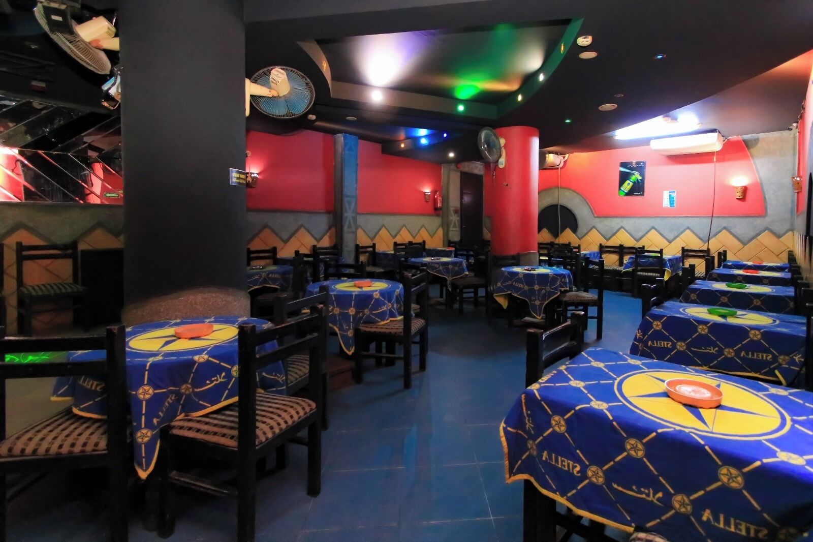 Un restaurante con mesas cubiertas por manteles azules, paredes rojas y un reloj en la pared.
