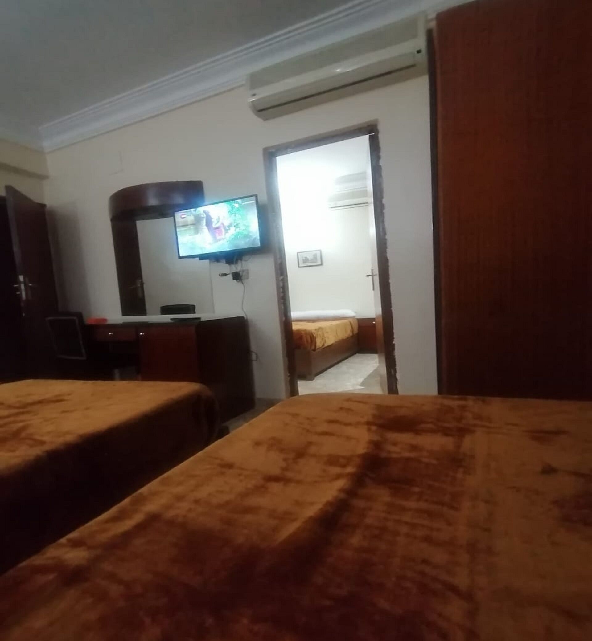 A hotel room with two beds, a TV mounted on the wall, and a door leading to another room.