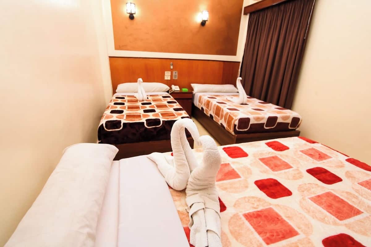 Ein Hotelzimmer mit drei Betten, jedes mit einer anderen gemusterten Bettdecke. Zwei Wandleuchten befinden sich über den Betten.