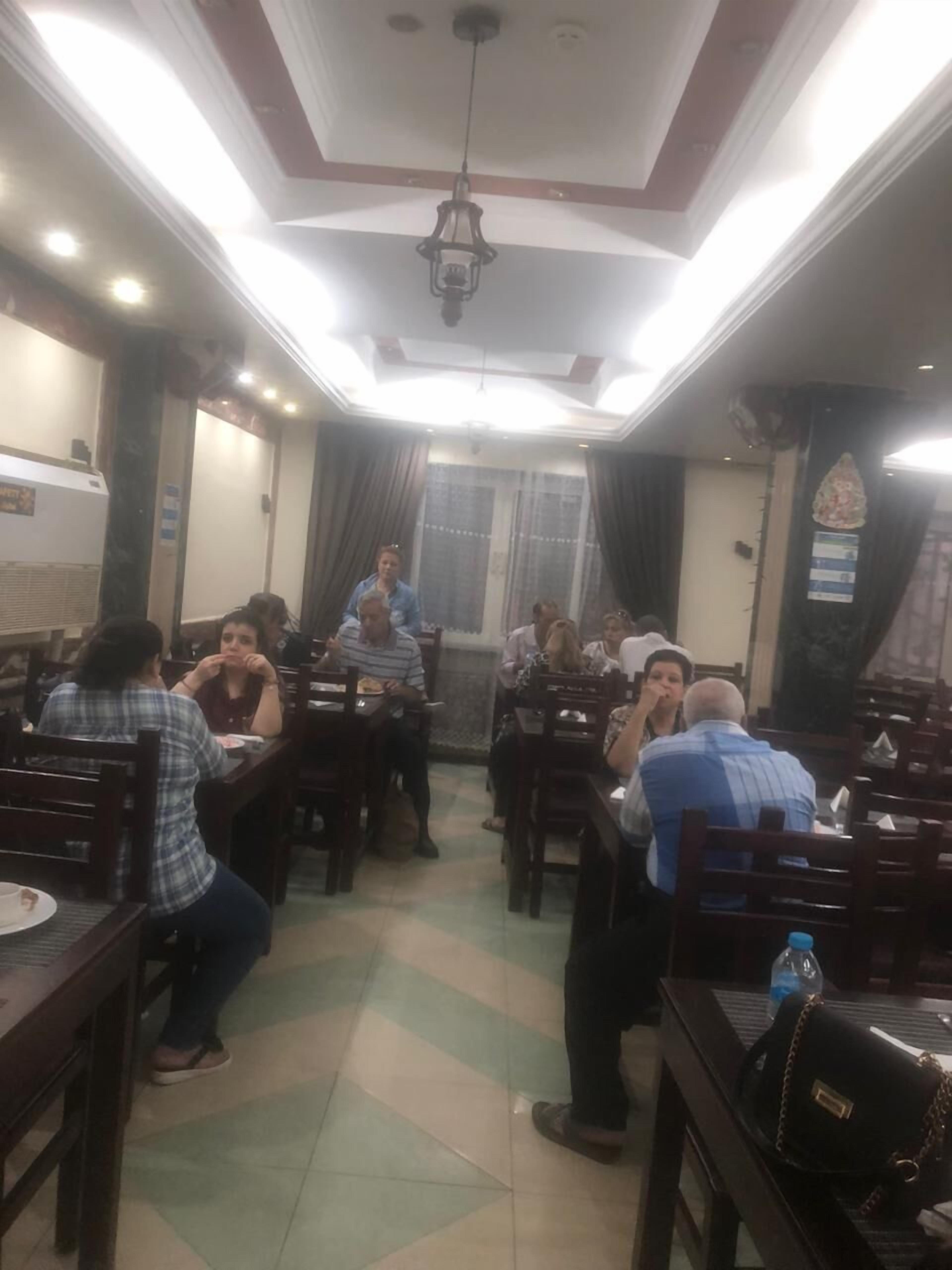 A restaurant with wooden tables and chairs, a tiled floor, and a ceiling with recessed lighting.