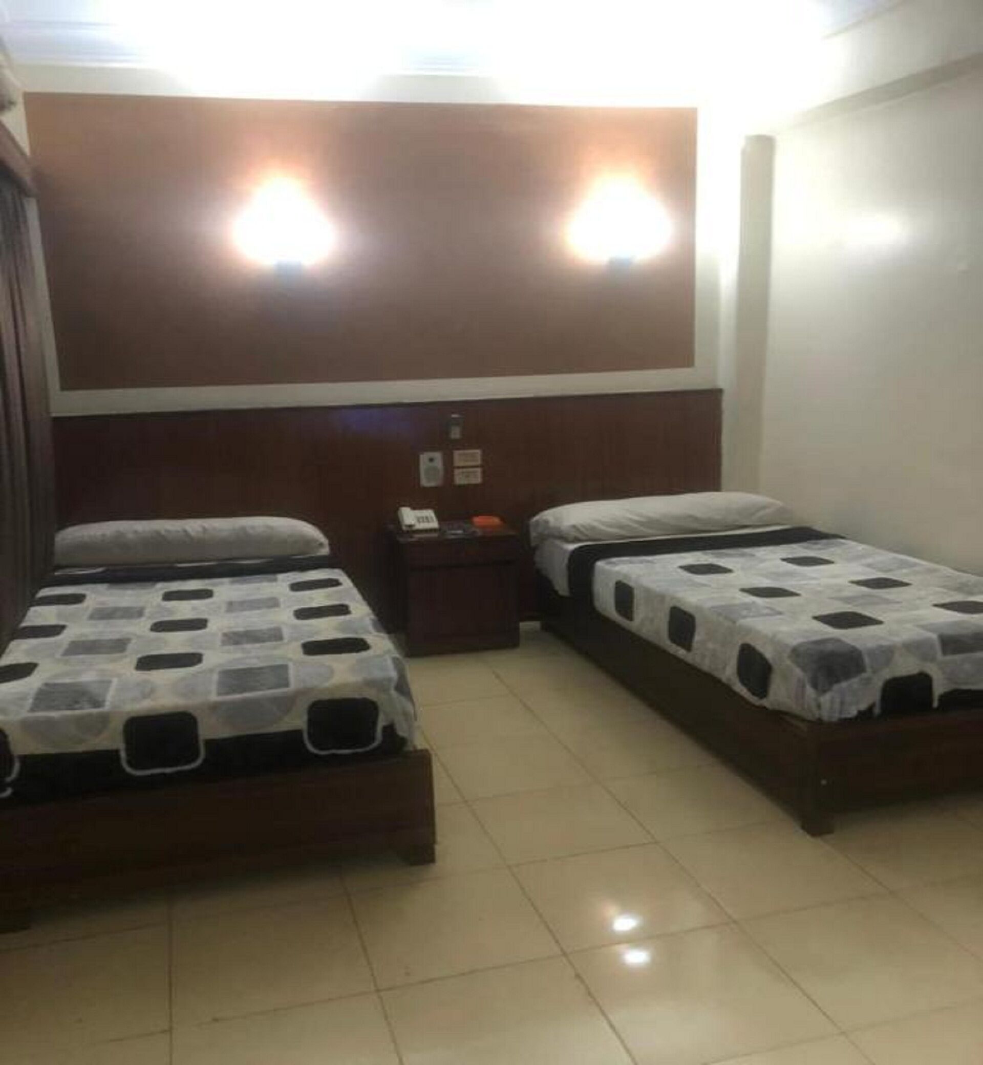 Una habitación de hotel con dos camas individuales, una mesita de noche y un cabecero de madera.