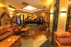 Eine Hotlellobby mit Rezeption, einer Sitzecke mit Sofas und Sesseln, einem Couchtisch und einer dekorativen Decke.