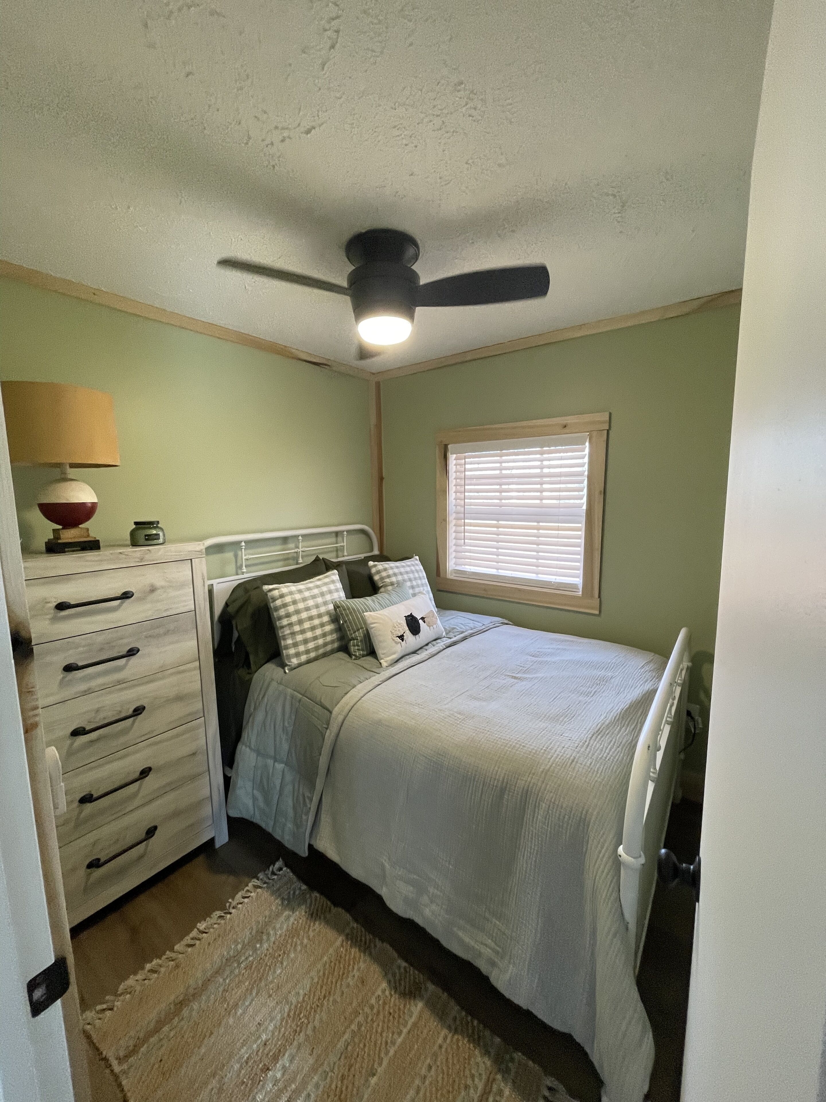 A bedroom with a bed, a dresser, a lamp, and a ceiling fan.