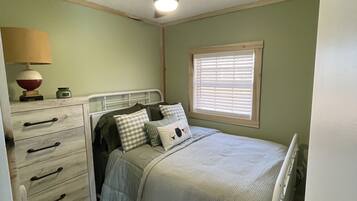A bedroom with a bed, a dresser, a lamp, and a ceiling fan.