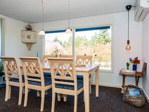 Uma sala de jantar com mesa e cadeiras de madeira, janela com vista para árvores e ar-condicionado fixado na parede.