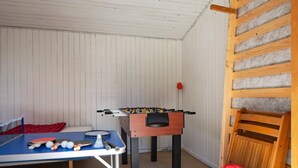 A room with a foosball table, a ping pong table, and a small table with badminton rackets.