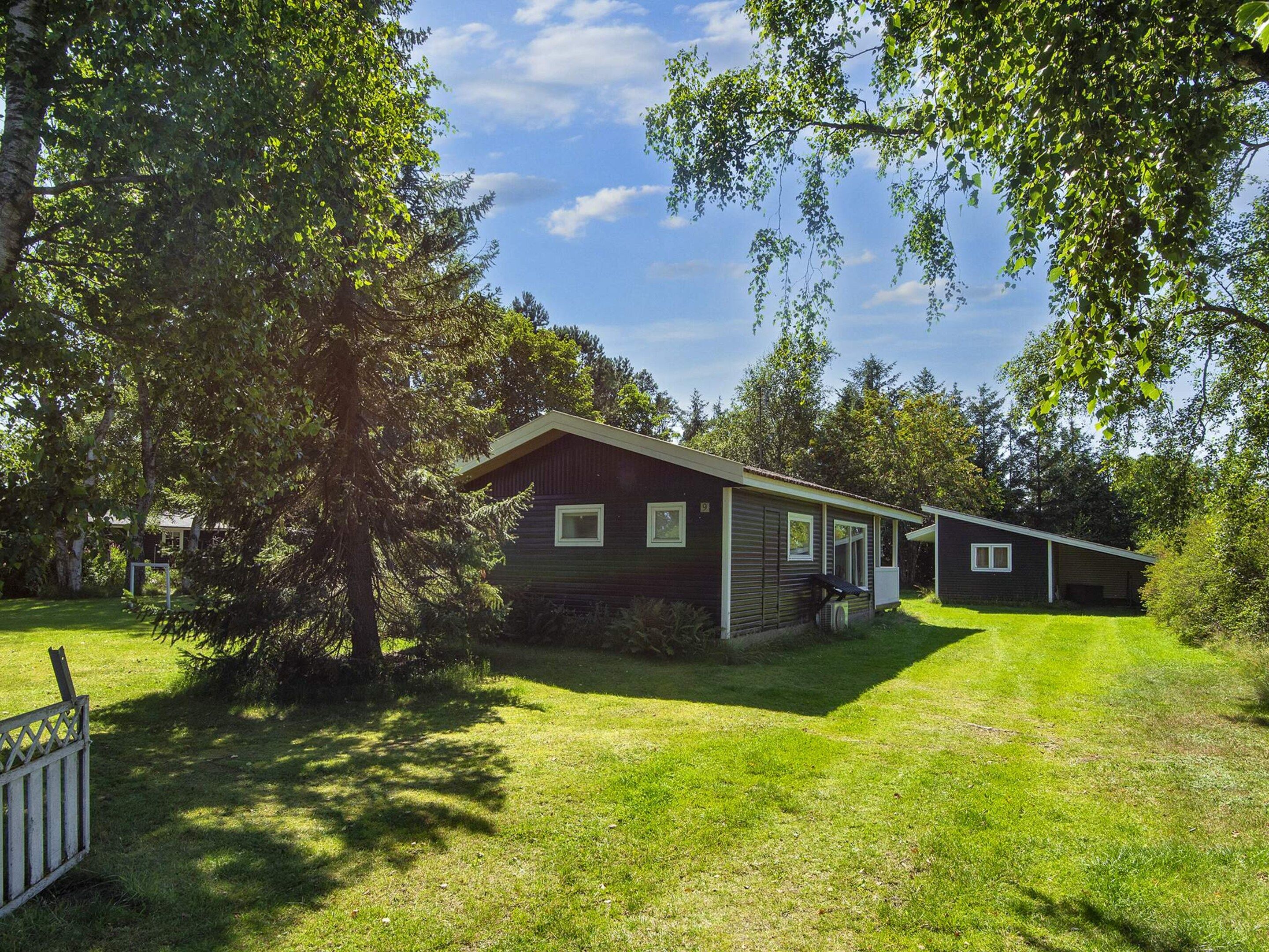 A single-story cabin with a sloped roof, surrounded by a well-maintained lawn and dense trees.