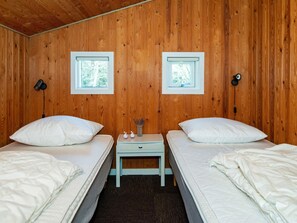 A room with two beds, wooden walls, two windows, a nightstand with a lamp, and a small table with decorative items. - 6 Person Holiday Home in Glesborg (Glesborg)