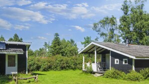 A rustic cabin with a porch and a small deck, surrounded by lush greenery and trees.